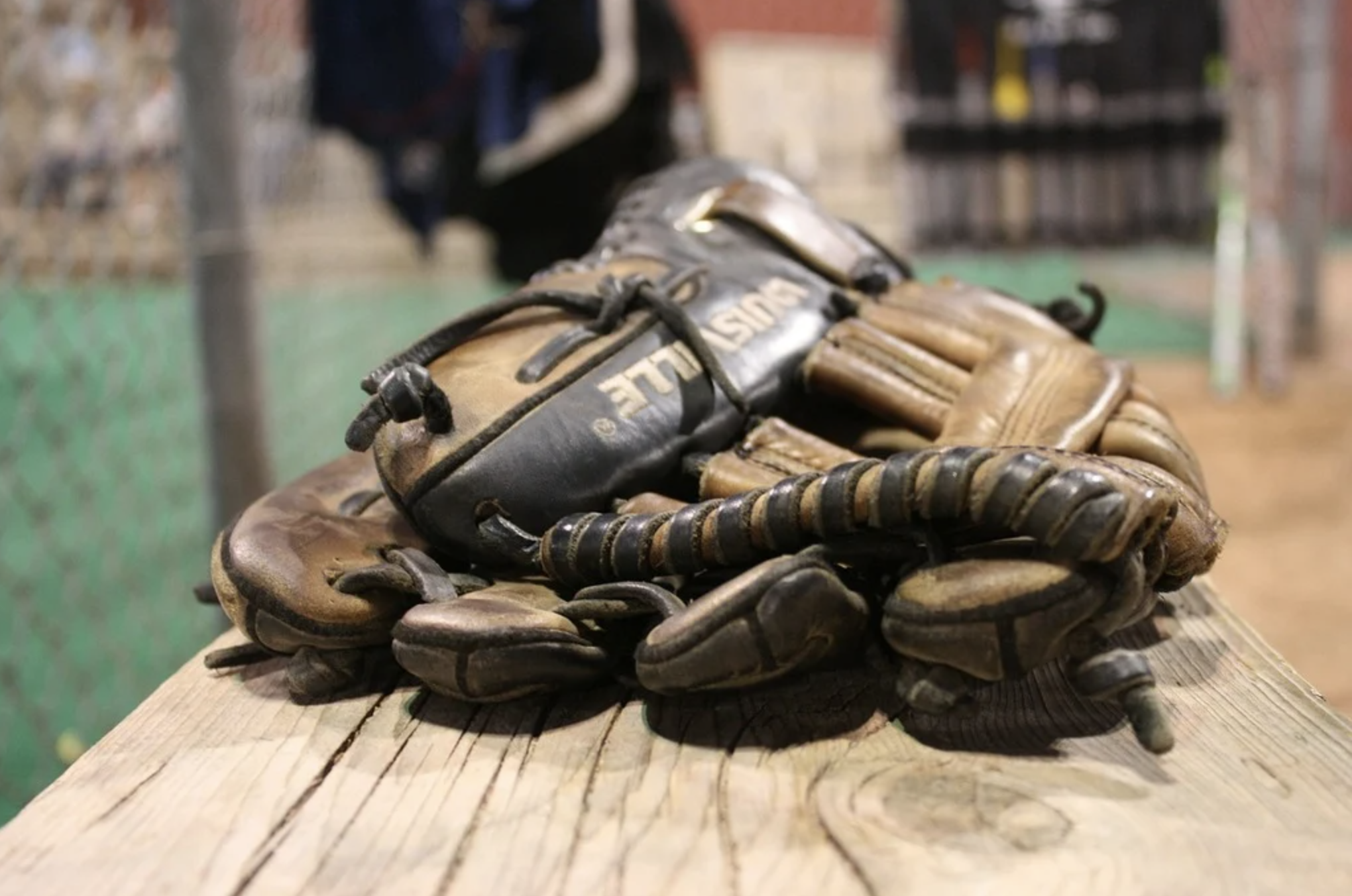 Stack of well-worn baseball gloves on dugout bench